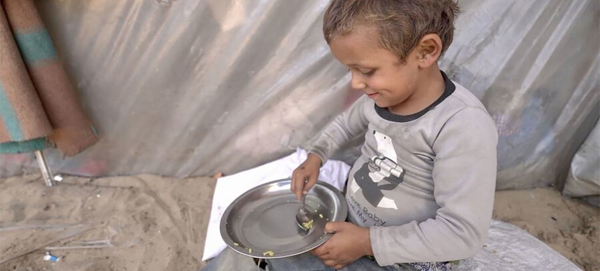 Um menino recolhe os últimos grãos de arroz de sua tigela. A fome está aumentando em Gaza.