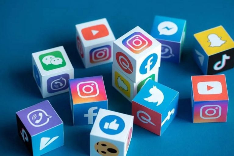 Imagem ilustrativa de cubos tridimensionais espalhados sobre um fundo azul, cada cubo possui em seus lados os logos de uma rede social